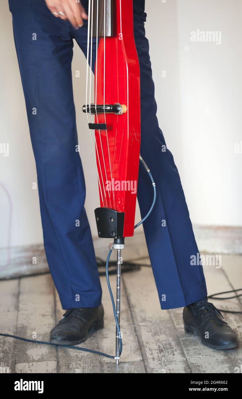 Ein Mann spielt roten elektrischen Kontrabass im Musikstudio, Nahaufnahme vertikale Foto mit selektivem Fokus. Live-Musik im Hintergrund Stockfoto