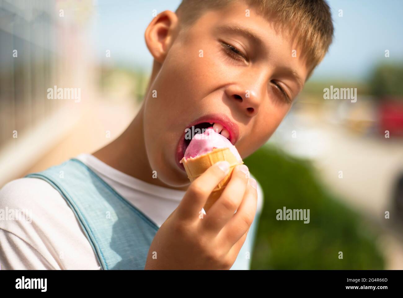 Der Junge isst Eis. Eiscreme mit rosa Erdbeeren in einem Waffelbecher. Genuss. Leckeres Eis. Stockfoto Der Junge isst Eis. Eiscreme mit rosa Erdbeeren in einem Waffelbecher. Genuss. Leckeres Eis. Stockfoto