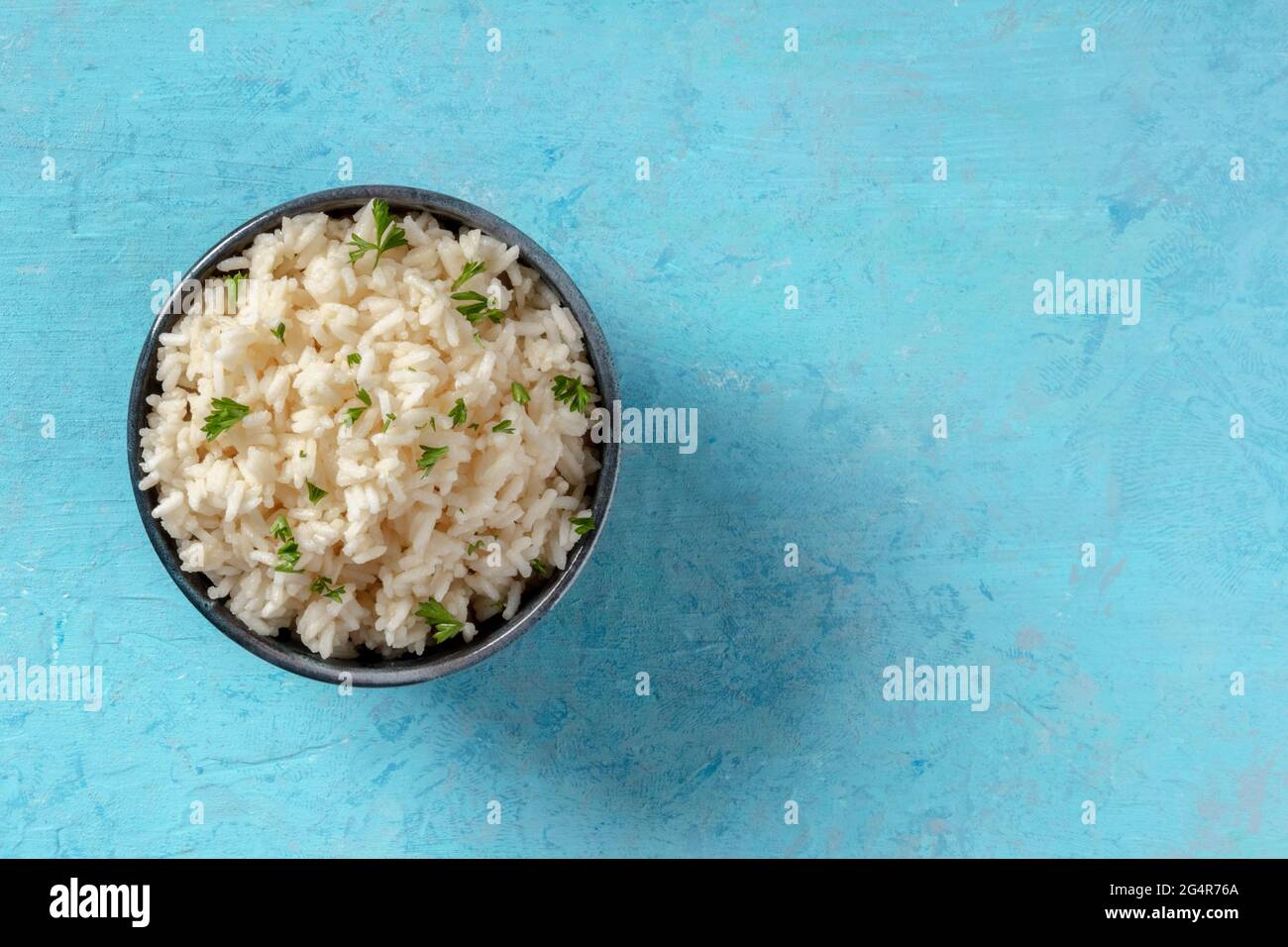 Reis mit Petersilienblättern, obere Aufnahme auf blauem Hintergrund mit Platz für Text Stockfoto