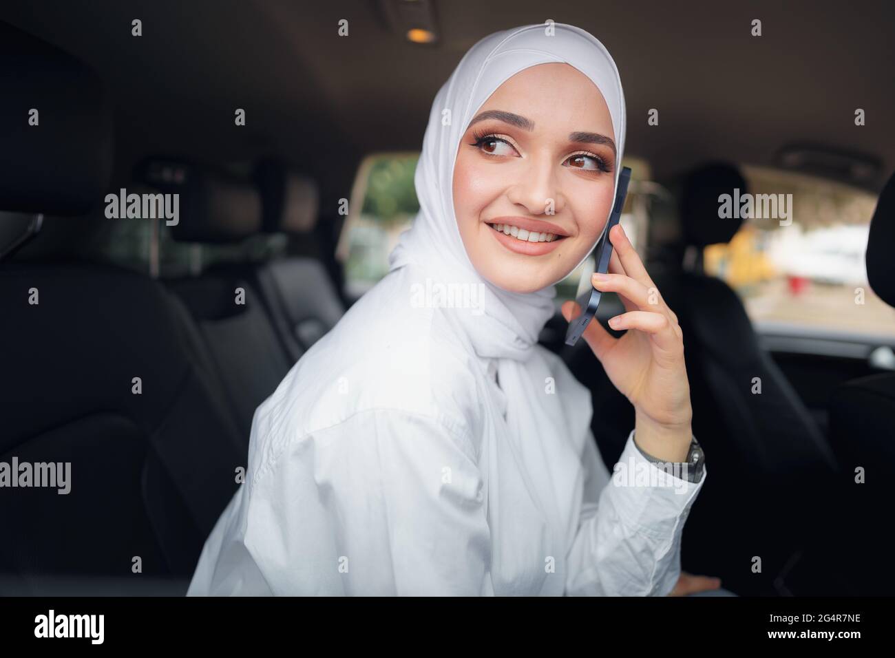 Schöne junge Frau im Hijab sitzt in einem Auto und spricht am Telefon Stockfoto