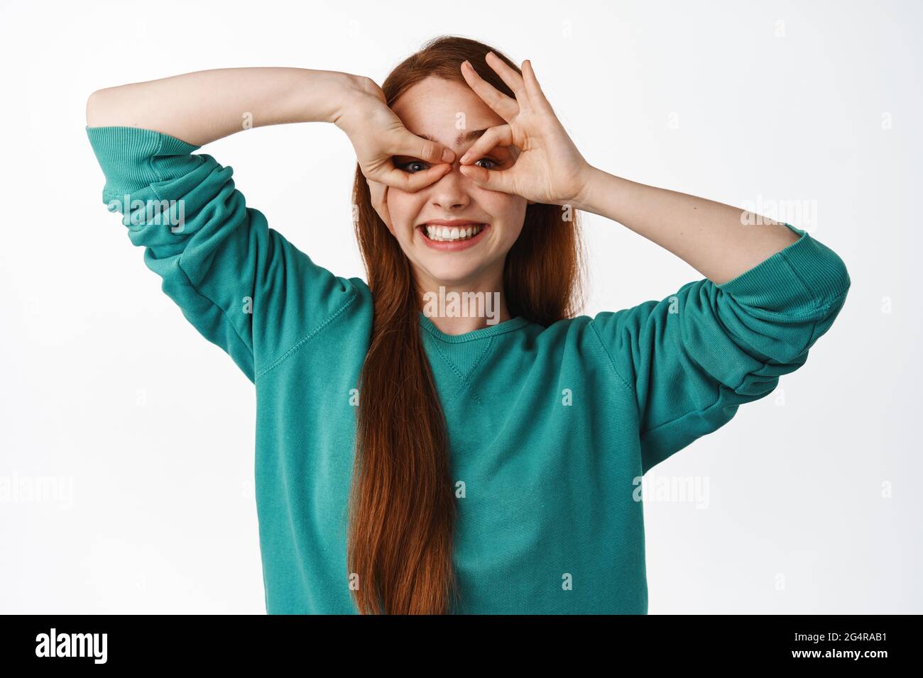 Happy Ingwer Mädchen schaut durch Finger Brille Fernglas, lächelt glücklich  und positiv, macht Superhelden Maske und spielen, über weiß stehen  Stockfotografie - Alamy