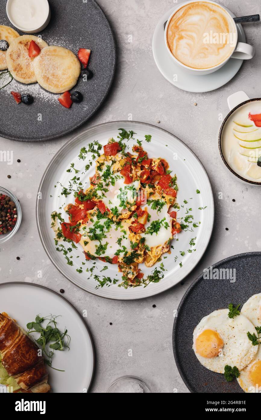 Verschiedene Frühstücksoptionen. Rührei, Käsekuchen, Milchbrei, Kaffee Stockfoto