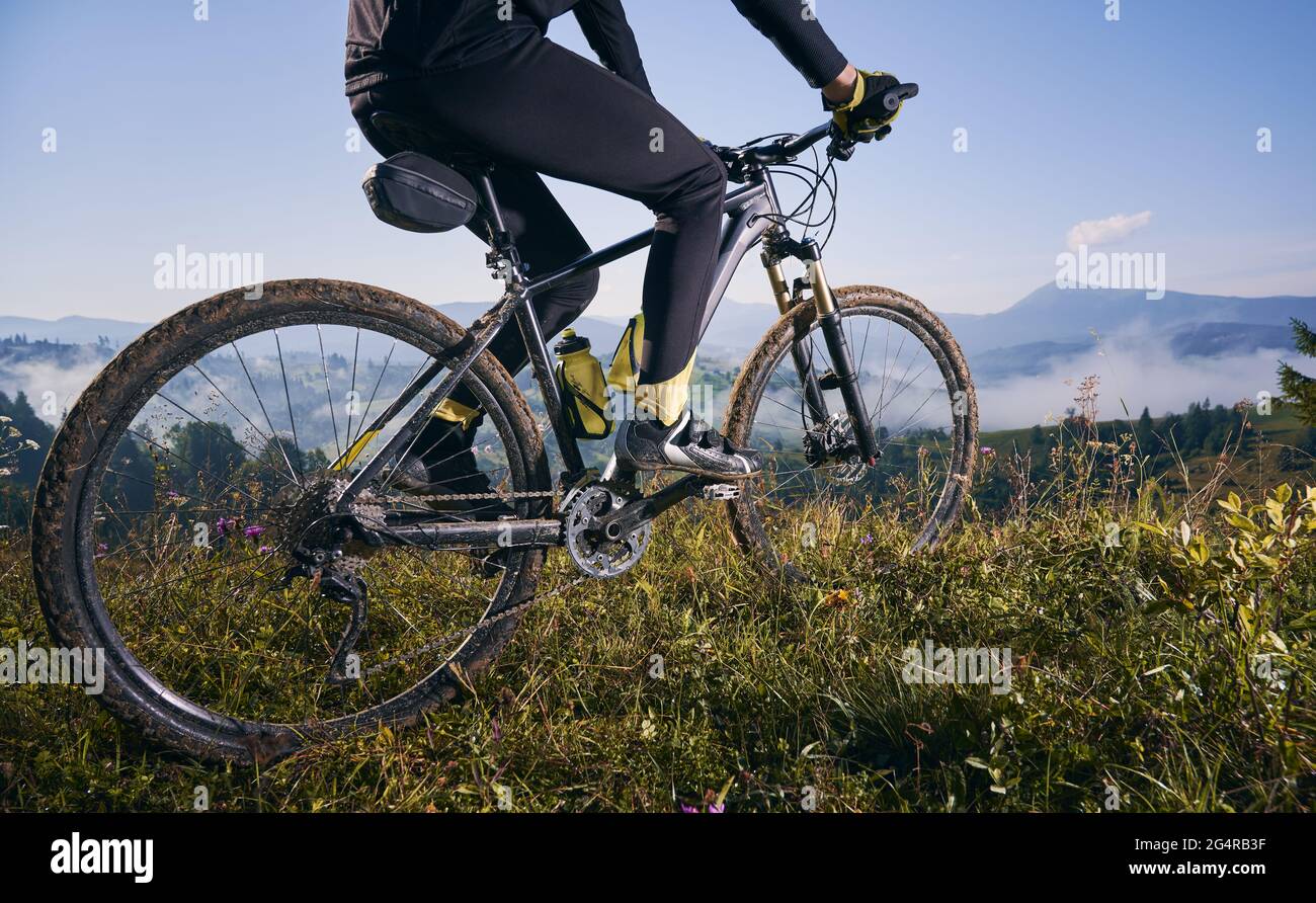 Nahaufnahme, niedriger Winkel auf einem Fahrrad mit Radfahrer. Die Beine des Mannes reiten im Sommer auf Gras in den Bergen gegen den blauen Himmel. Konzept des Extremfahrens Stockfoto