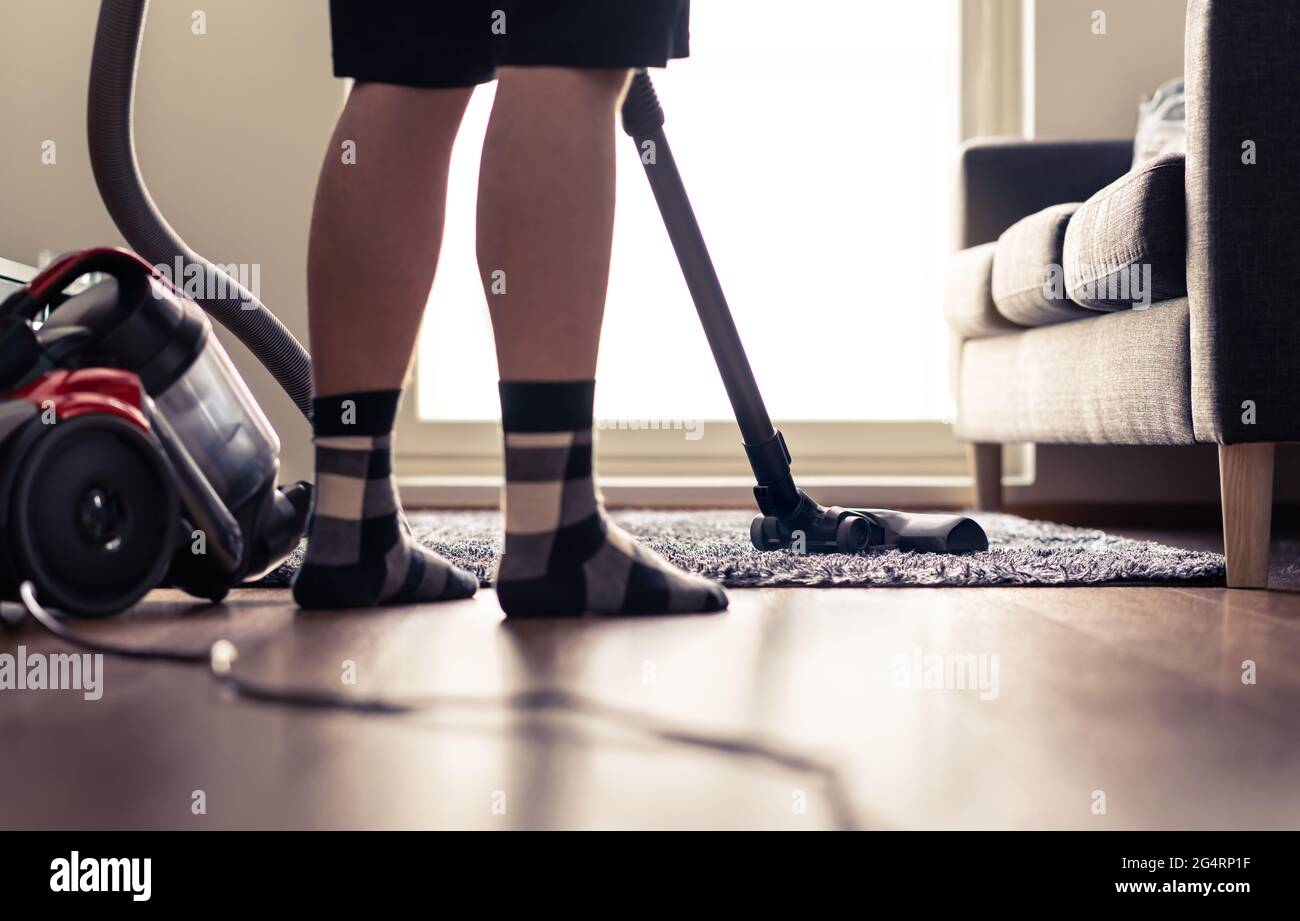 Mann reinigt Teppich und Boden mit Staubsauger zu Hause. Glückliche Person, die den Teppich im Wohnzimmer saugt. Ordentliches Haus. Hausarbeiten in modernen Wohnung. Stockfoto