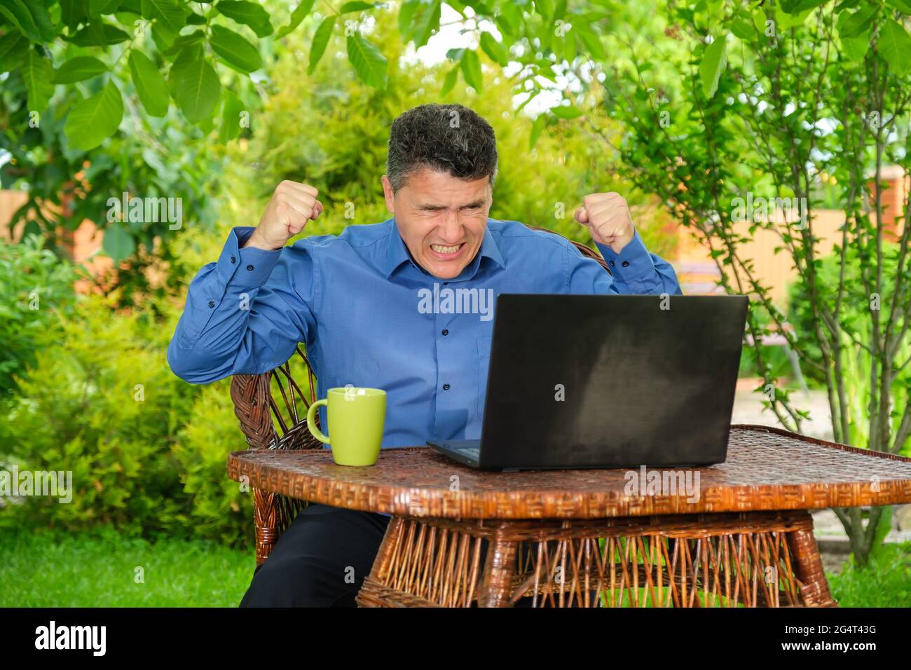 Wütender Geschäftsmann klatscht Fäuste und knirscht seine Zähne in der Nähe des Laptops im Hinterhof Stockfoto