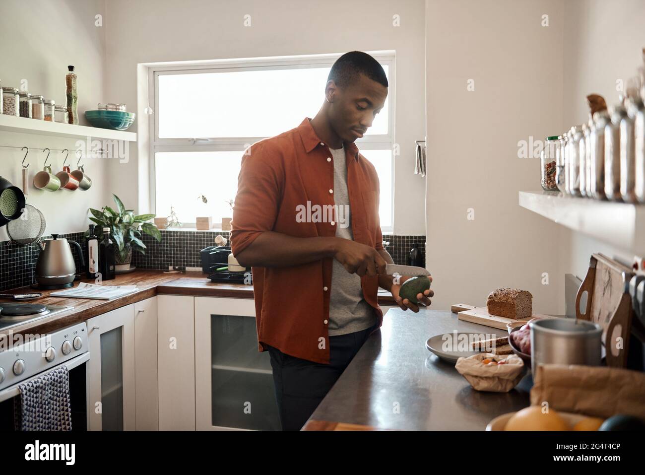 Junger afrikanischer Mann, der in seiner Küche eine Avocado schneidet Stockfoto
