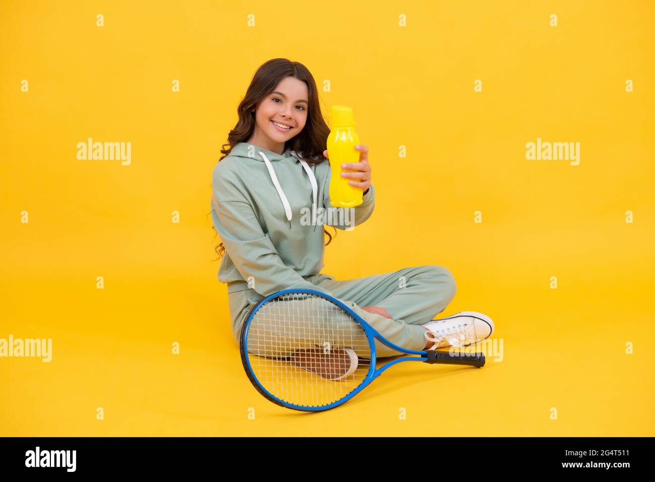 Kind sitzen mit Schläger und Wasserflasche. Kind mit Tennisschläger. Teen Mädchen trinken Wasser Stockfoto
