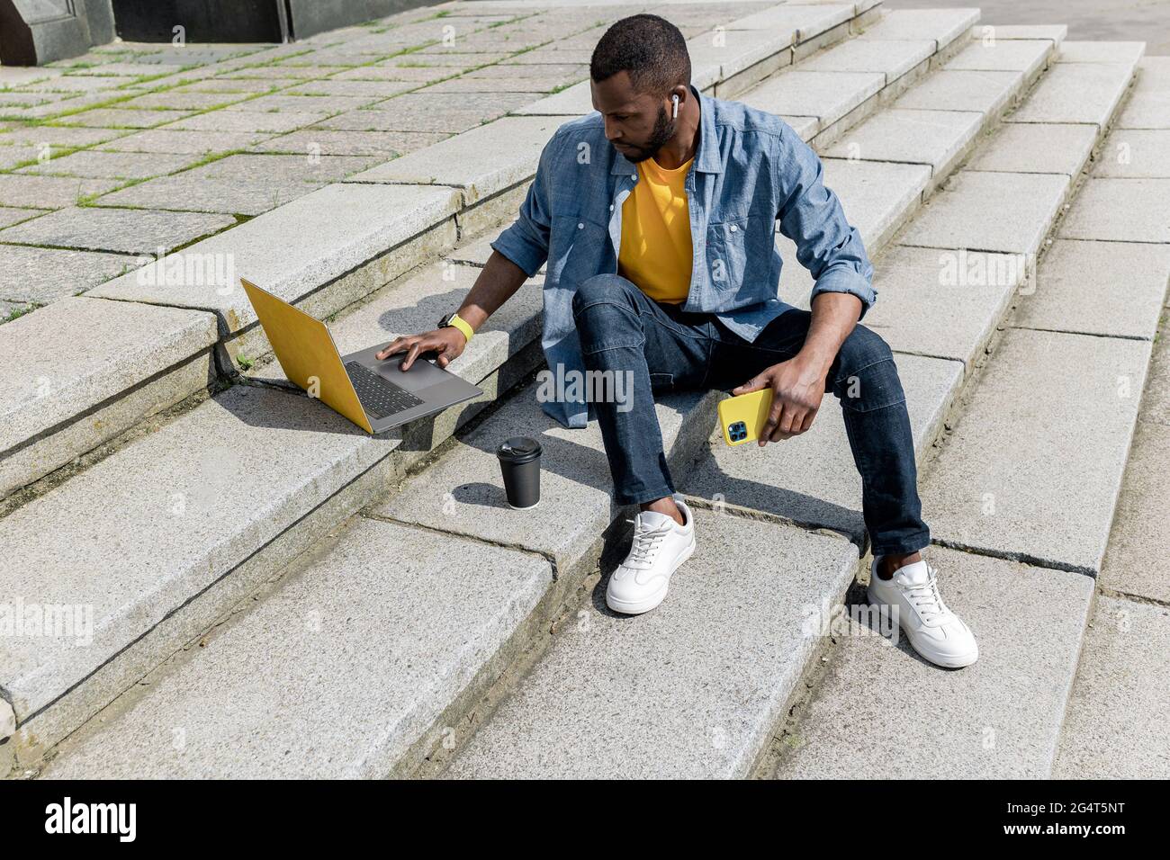 Junge konzentriert stilvolle afroamerikanische freiberufliche Geschäftsmann männlich arbeiten mit Laptop und Handy im Freien, auf der Treppe sitzen Stockfoto