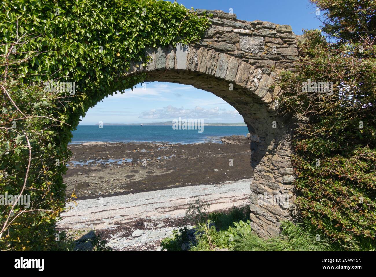 Ein Blick auf das Meer durch einen Steinbogen, der in Holyhead bei einem Spaziergang auf dem Isle of Anglesey Coastal Path, Wales, Großbritannien, angetroffen wurde Stockfoto