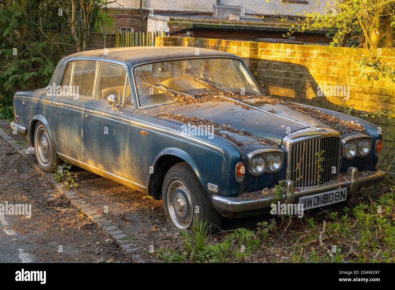 Verlassene Bentley-Autos, die neben einer Straße rosten, beleuchtet durch Abendlicht Stockfoto