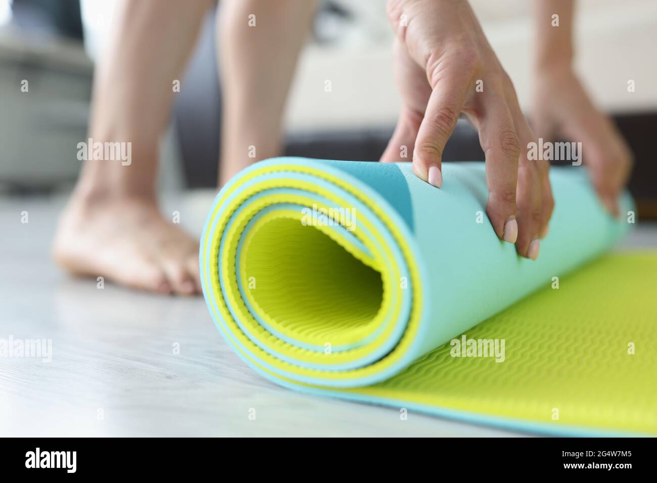 Frau faltet Yoga- oder Fitnessmatte nach dem Training zu Hause im Wohnzimmer Stockfoto