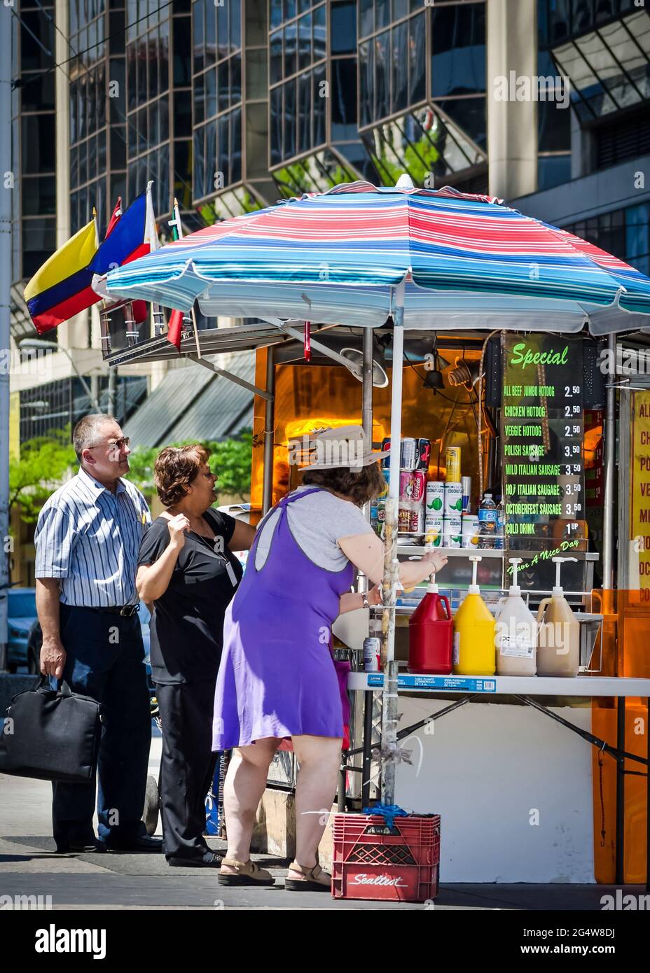Hot Dog Stand Downtown Toronto:Frau Straßenverkäufer, die Essen und Getränke am Straßenrand verkauft, mit ihrem Wagen, der unter einem bunten Regenschirm platziert ist, ein Mann und ein Mann Stockfoto