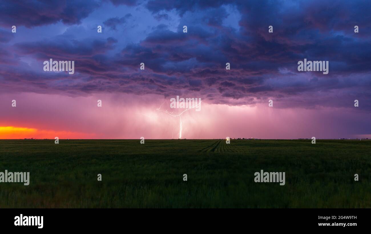 Blitzschläge treffen in der Dämmerung an der Grenze zu Wyoming/Colorado mit dunklen Sturmwolken darüber ein. Am Horizont ist der orange Schein des Sonnenuntergangs zu sehen. Stockfoto