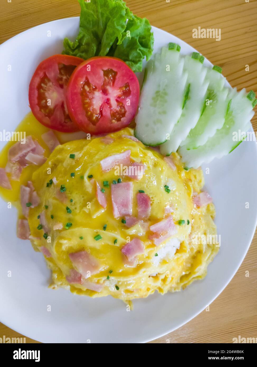 Jasminreis mit Schinken-Omelette, serviert mit den Tomaten- und Gurkenschiebern auf der sauberen weißen Platte im lokalen Restaurant, oberhalb mit dem CO Stockfoto