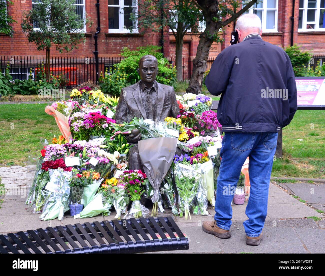Blumen umgeben die Alan Turing Statue und das Denkmal, Sackville Gardens, Manchester, England, Großbritannien, Vereinigtes Königreich, am 23. Juni 2021, dem Jahrestag von Turing's Geburtstag. Alan Mathison Turing OBE war ein englischer Mathematiker, Informatiker, Logiker und Kryptanalyst. Im 2. Weltkrieg leitete er ein Team, das dafür verantwortlich war, deutsche Cipher der Enigma-Maschine zu brechen. Turing hatte damals Einfluss auf die Entwicklung der Informatik an der University of Manchester. Stockfoto