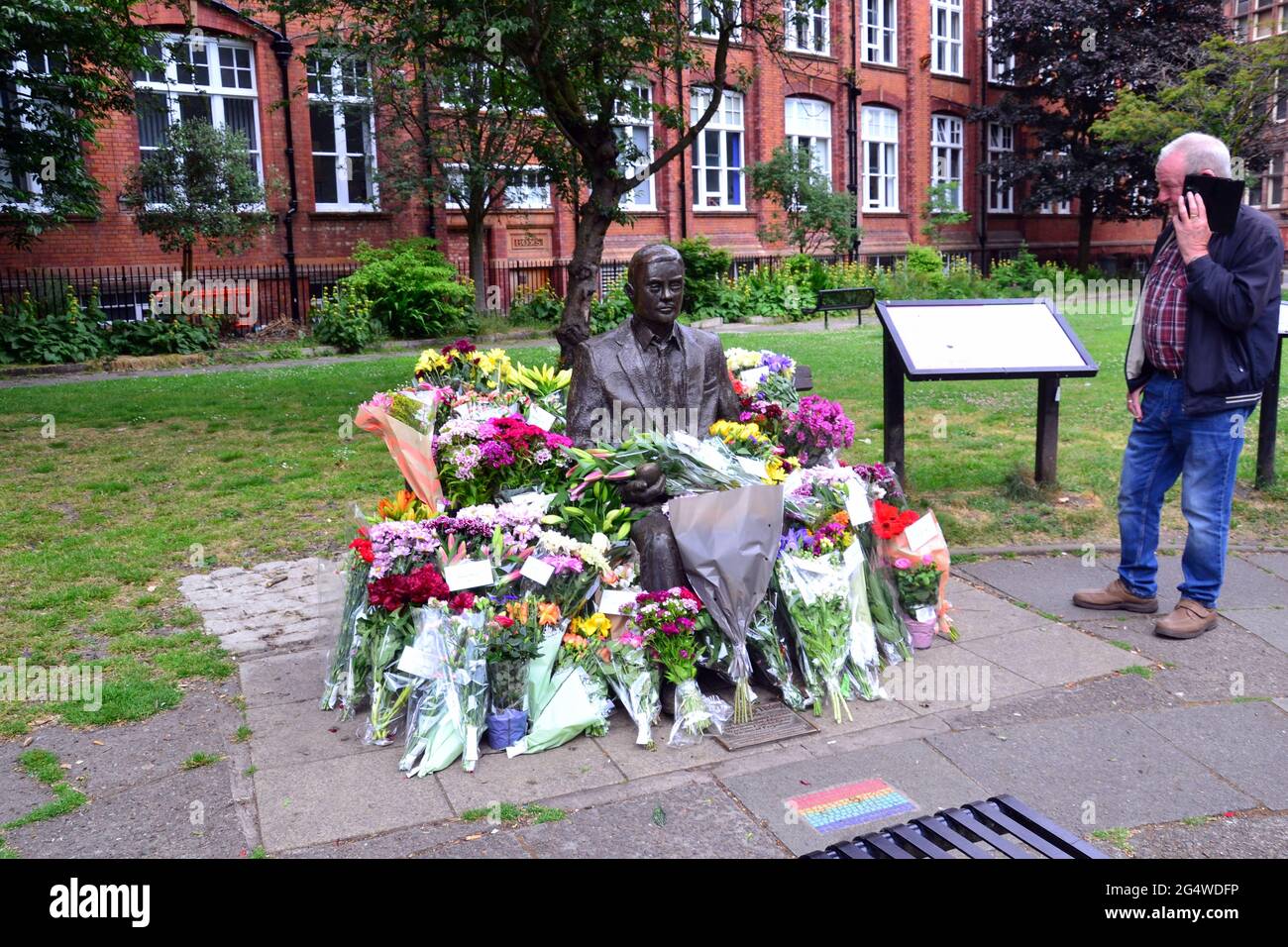 Blumen umgeben die Alan Turing Statue und das Denkmal, Sackville Gardens, Manchester, England, Großbritannien, Vereinigtes Königreich, am 23. Juni 2021, dem Jahrestag von Turing's Geburtstag. Alan Mathison Turing OBE war ein englischer Mathematiker, Informatiker, Logiker und Kryptanalyst. Im 2. Weltkrieg leitete er ein Team, das dafür verantwortlich war, deutsche Cipher der Enigma-Maschine zu brechen. Turing hatte damals Einfluss auf die Entwicklung der Informatik an der University of Manchester. Stockfoto