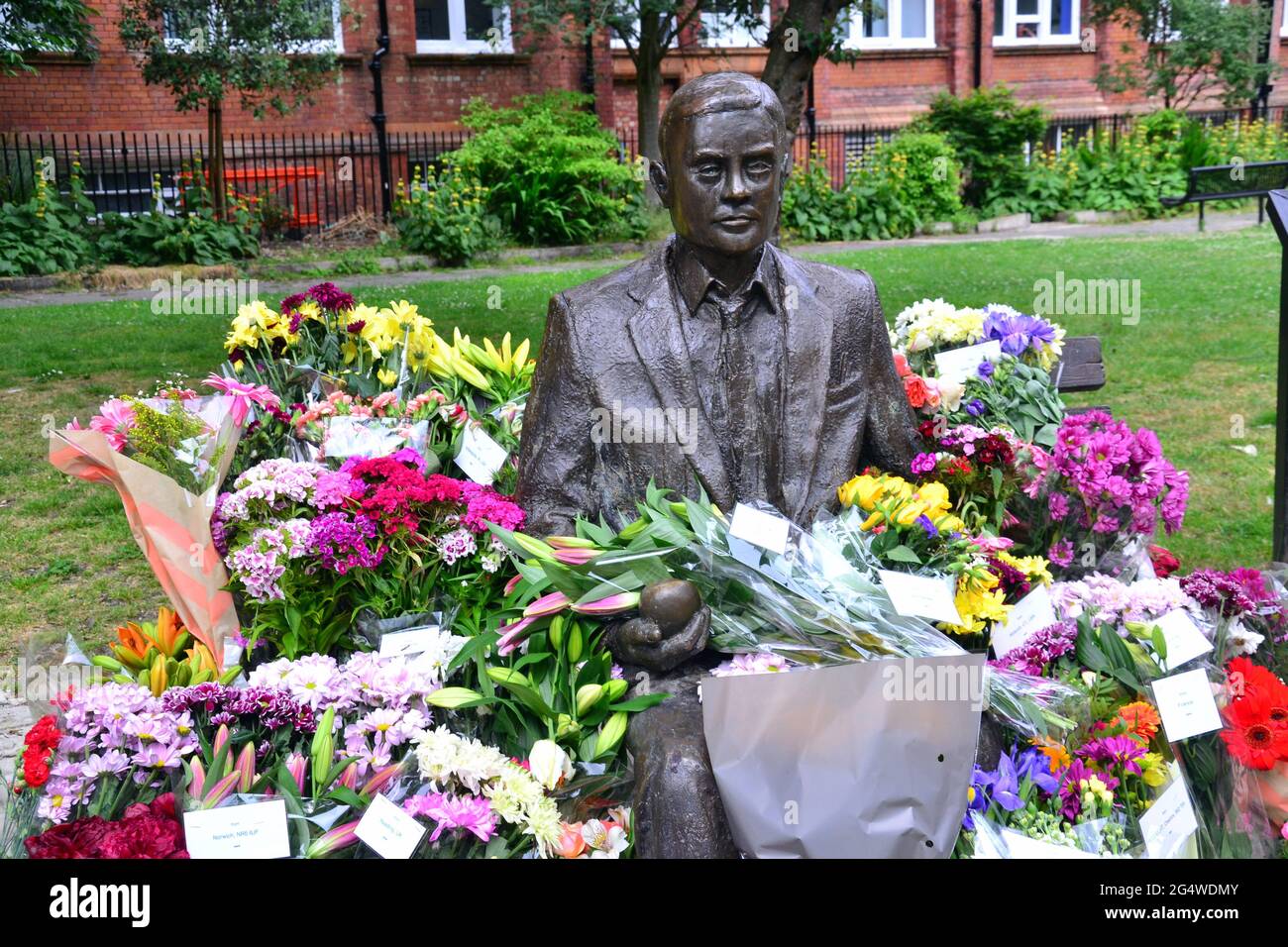 Blumen umgeben die Alan Turing Statue und das Denkmal, Sackville Gardens, Manchester, England, Großbritannien, Vereinigtes Königreich, am 23. Juni 2021, dem Jahrestag von Turing's Geburtstag. Alan Mathison Turing OBE war ein englischer Mathematiker, Informatiker, Logiker und Kryptanalyst. Im 2. Weltkrieg leitete er ein Team, das dafür verantwortlich war, deutsche Cipher der Enigma-Maschine zu brechen. Turing hatte damals Einfluss auf die Entwicklung der Informatik an der University of Manchester. Stockfoto