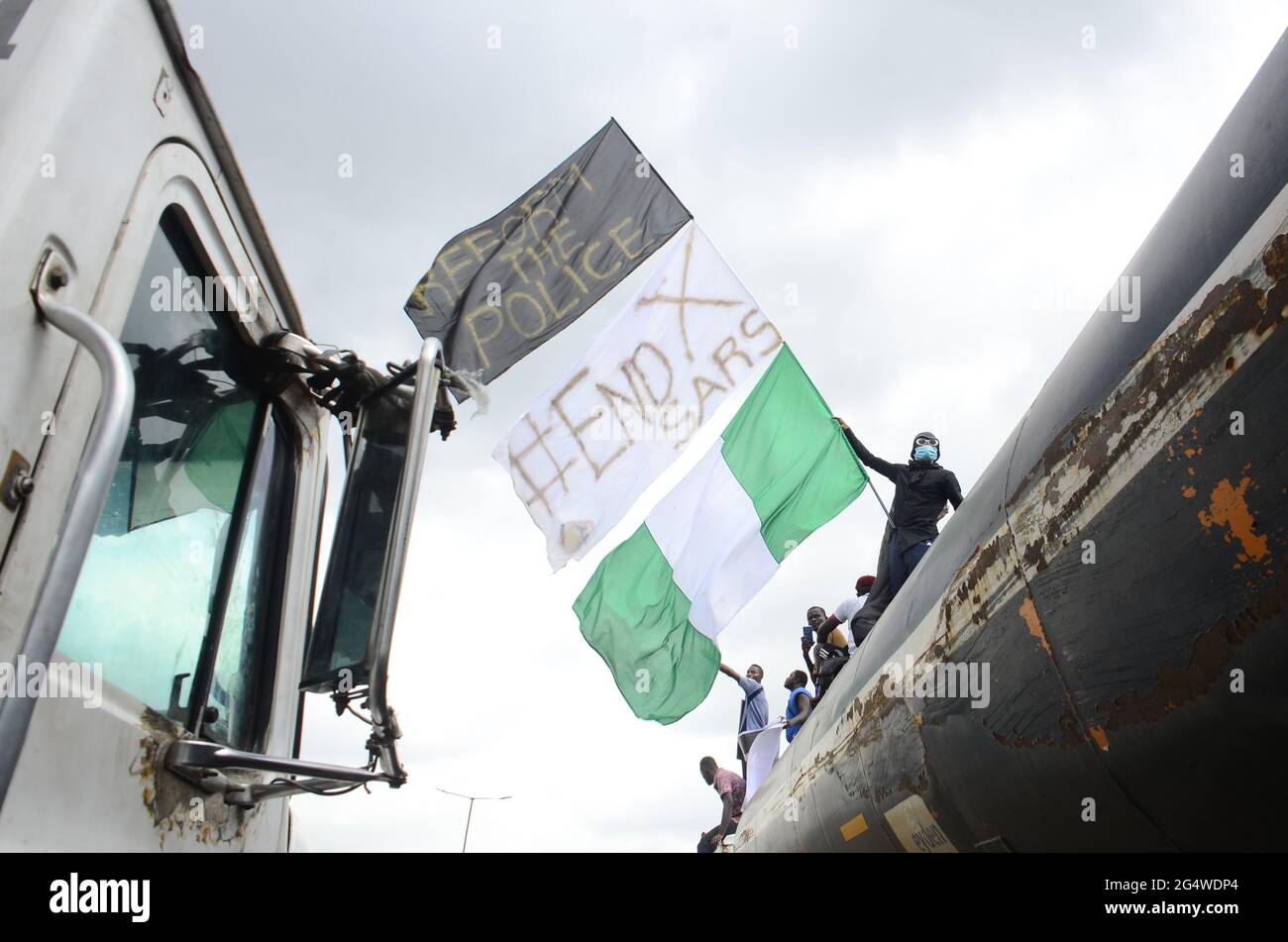 Jugendliche von ENDSARS-Demonstranten zeigen die nigrische Flagge und ein Plakat in einer Menschenmenge, um den anhaltenden Protest gegen die Belästigungen, Morde und Brutalität der nigrischen Polizeieinheit namens Special Anti-Raub Squad (SARS) im Parlamentsgebäude des Staates Lagos zu unterstützen. Lagos, Nigeria. Stockfoto