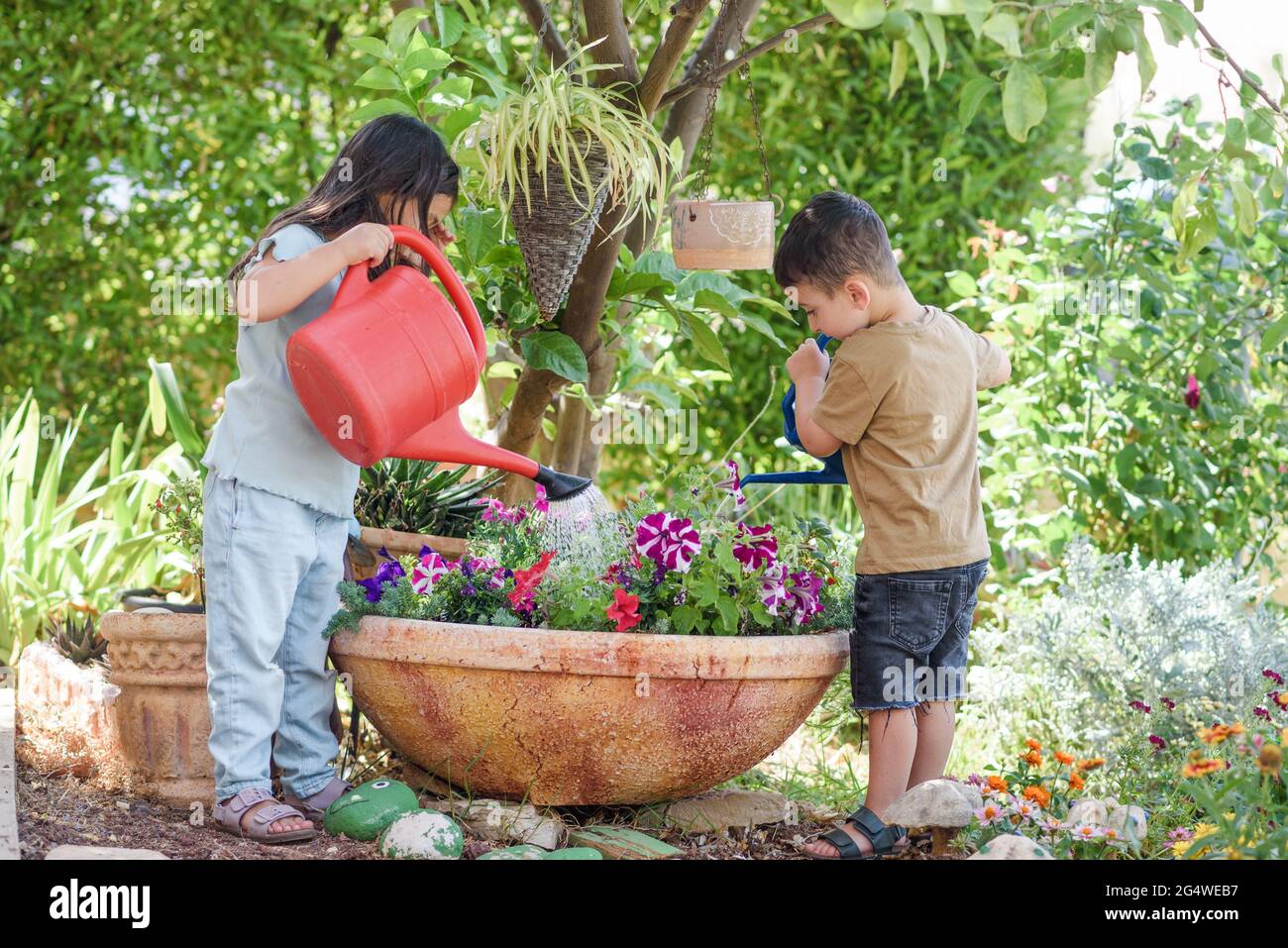 Kleine Mädchen und Jungen Pflanzen in nachhaltigen Tontöpfen in einem  Garten. Kinder, die Blumen im sonnigen Hinterhof bewässern Stockfotografie  - Alamy
