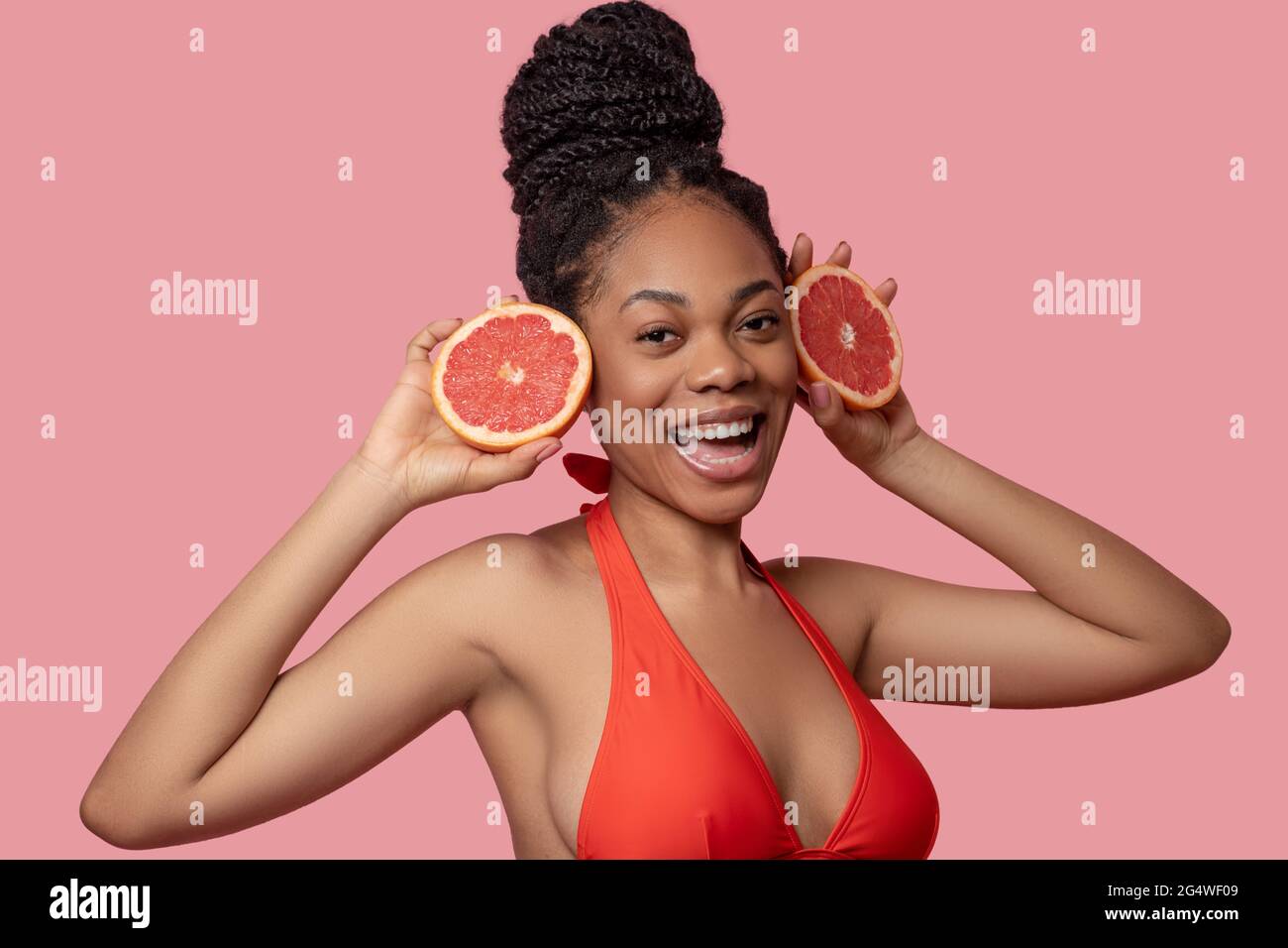 Dunkelhäutige Frau, die Grapefruitscheiben hält und glücklich aussieht Stockfoto