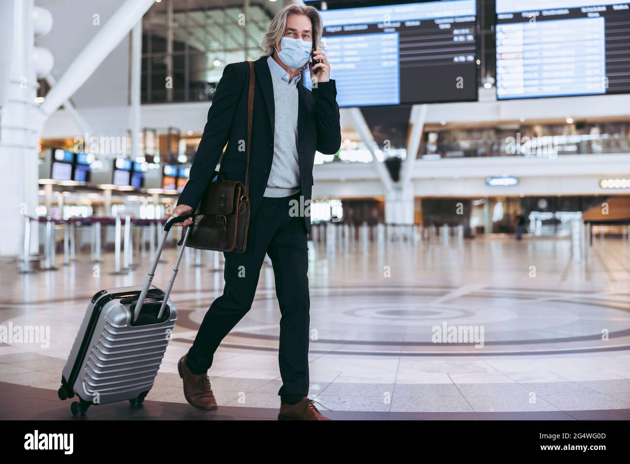 Geschäftsmann mit Gesichtsmaske und Telefongespräch, während er durch das Flughafenterminal ging. Mann auf Geschäftsreise nach der Sperrung einer Pandemie. Stockfoto