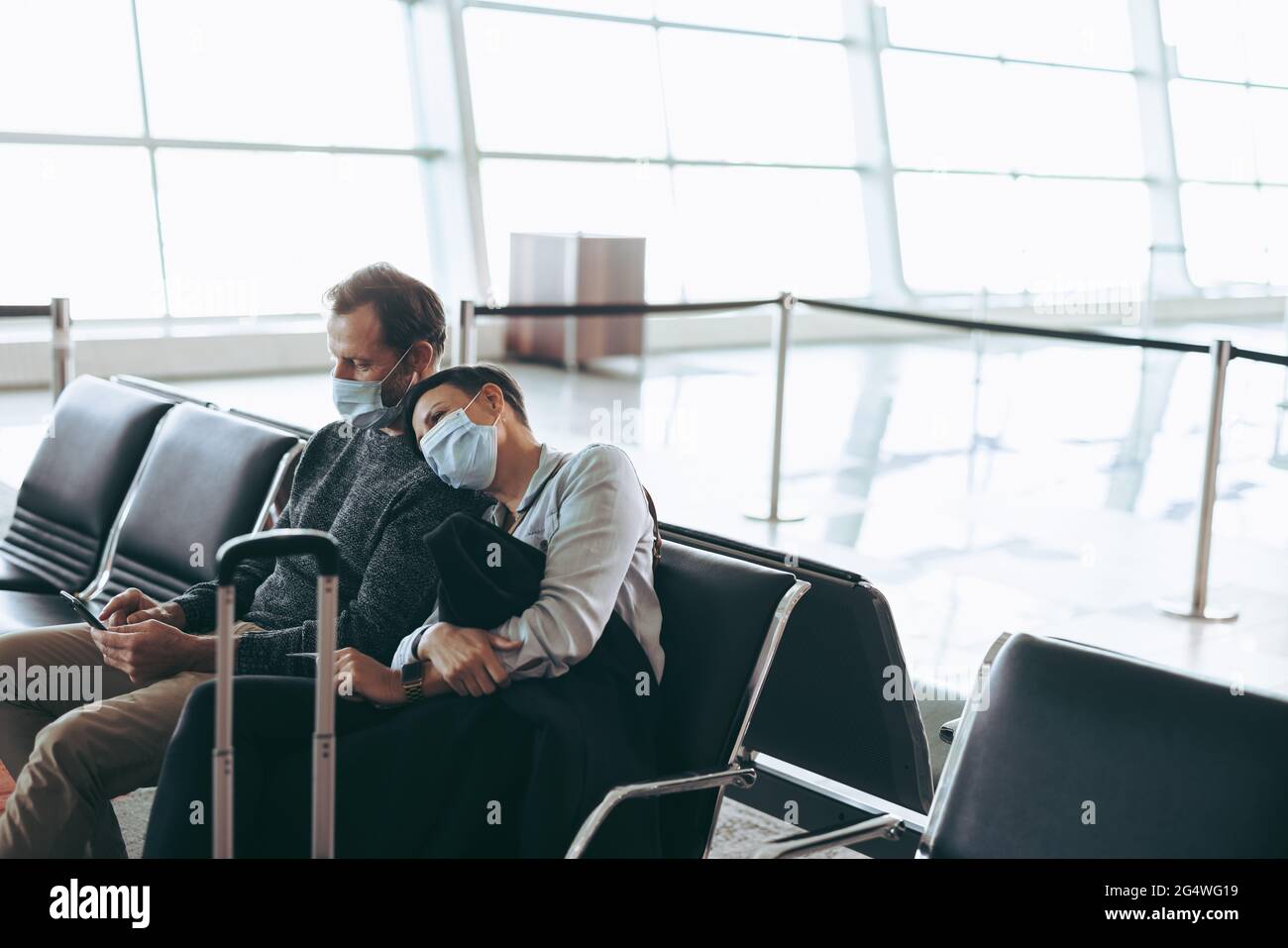 Passagierpaar in covid-19 Pandemie wartet am Flughafen. Tourist mit Gesichtsmasken, der im Wartebereich des Flughafenterminals sitzt. Stockfoto