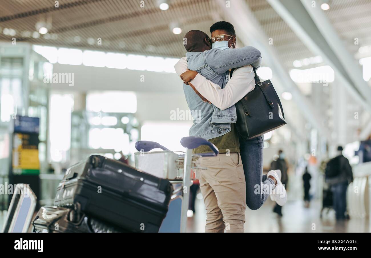 Afrikanischer Mann umarmt und hebt Frau am Flughafenterminal. Das Paar trifft sich nach langer Trennung am Flughafen nach der Sperrung durch eine Pandemie. Stockfoto