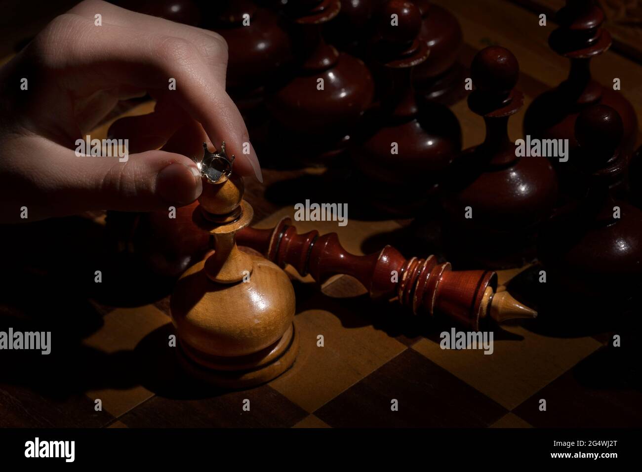Weibliche Hand hält einen Bauer mit einer Krone auf einem dunklen Hintergrund. Altes Schach. Geschäftskonzept Stockfoto