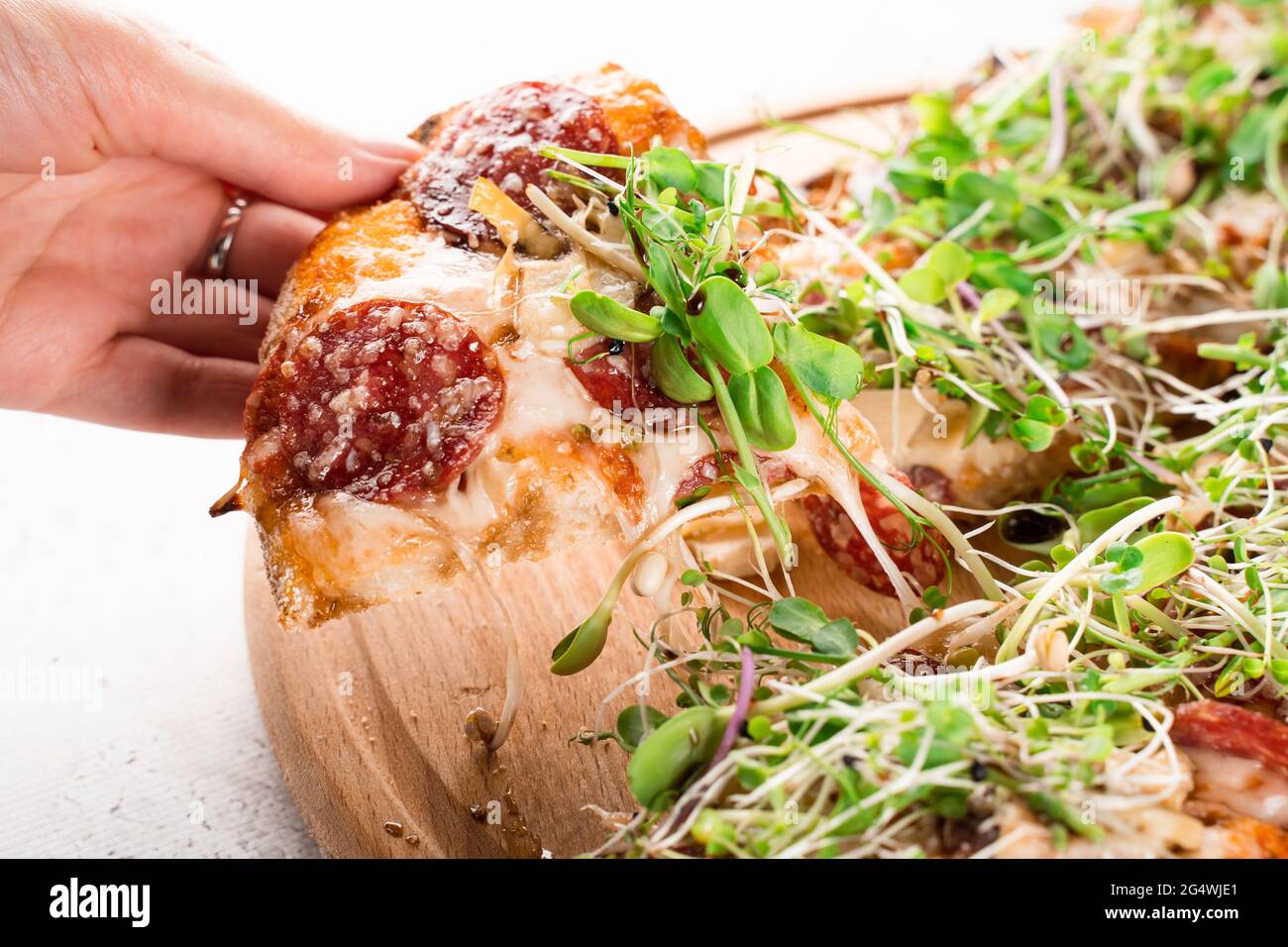 Stück Pinsa romana in der Hand mit streckenden Mozzarella mit Salami, Käse, Pilzen, verziert mit Microgreens auf Holzbrett. Stockfoto