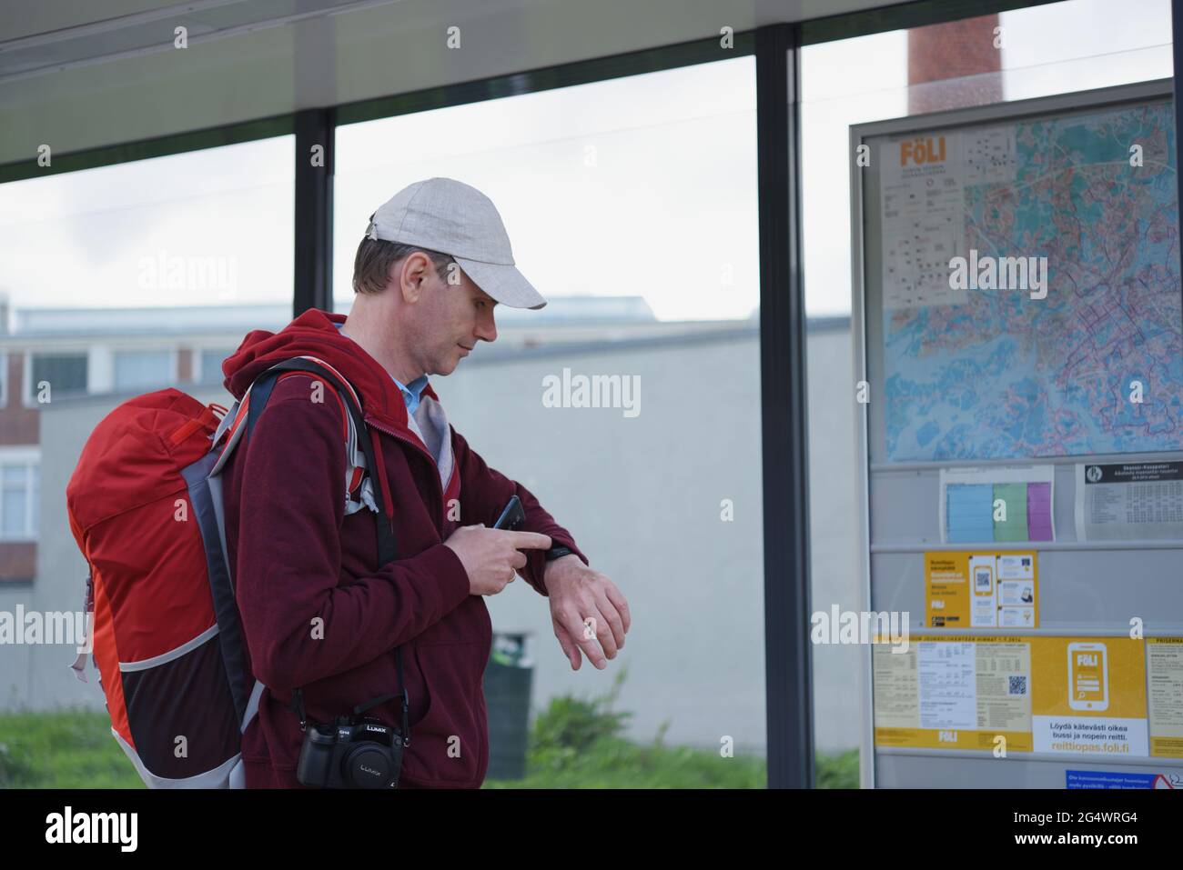 Reisender mit Rucksack und Kamera schaut auf seine Uhren an der Bushaltestelle in Turku, Finnland Stockfoto