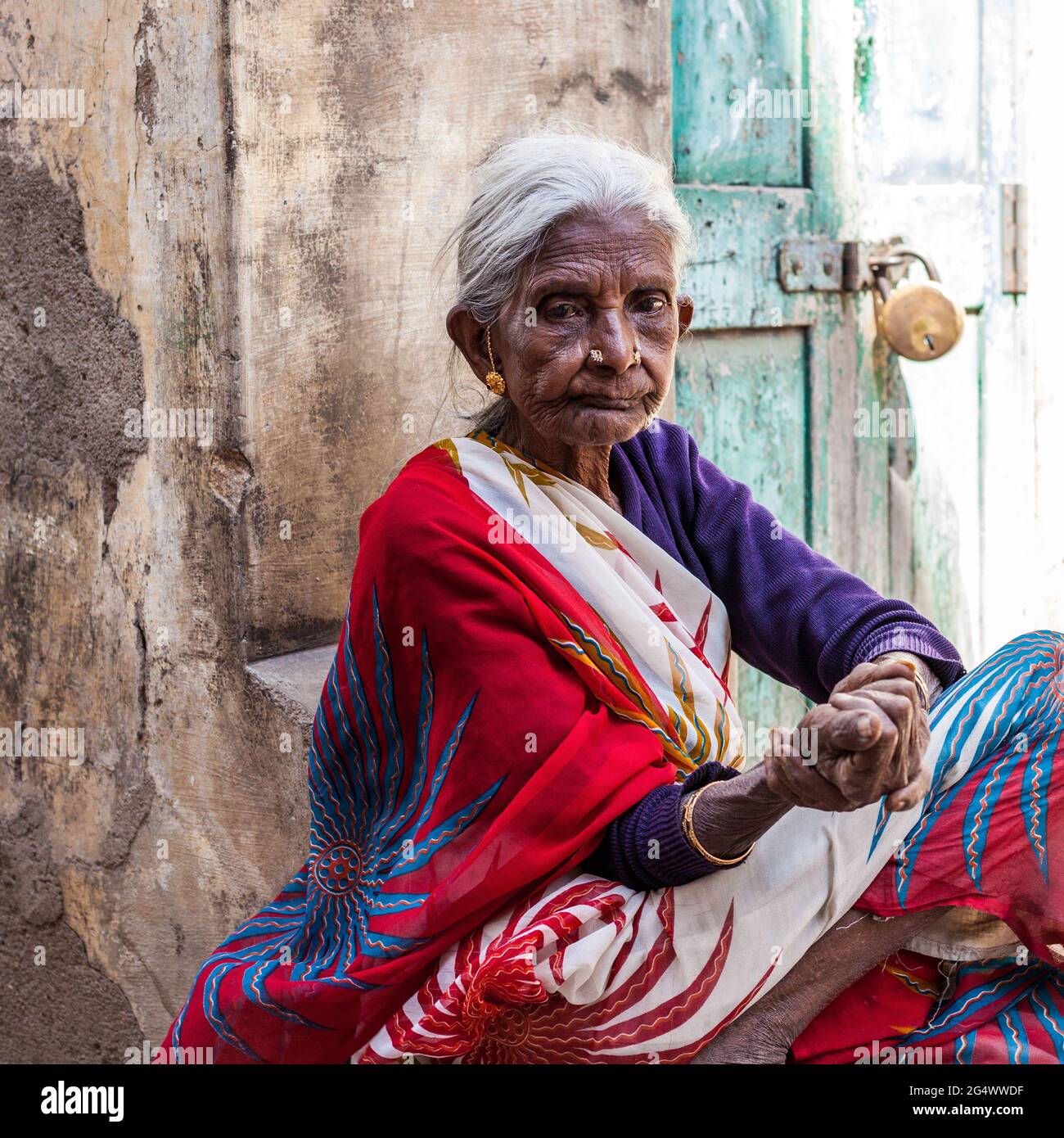 Nahaufnahme des Porträts einer älteren, nachdenklichen indischen Dame mit glasklaren Augen, die einen farbenfrohen Sari trägt, der vor dem Haus in Mysore, Karnataka, Indien, vor der Tür sitzt Stockfoto