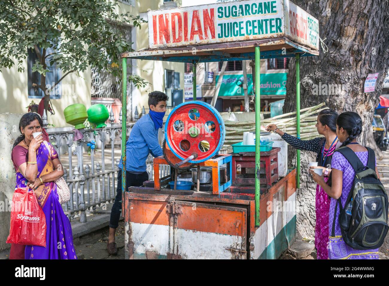 Indische Frauen trinken aus Getränken Stand mit Verkäufer mit Zuckerrohrsaft Maschine, Mysore, Karnataka, Indien Stockfoto