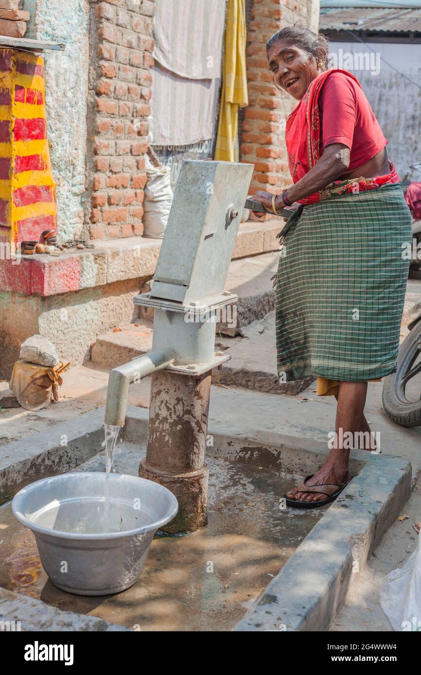 Indisches Weibchen mittleren Alters mit schlechten Zähnen Betelnussflecken pumpt Hebel am Straßenwasserbrunnen in Eimer, Trichy, Tamil Nadu, Indien Stockfoto
