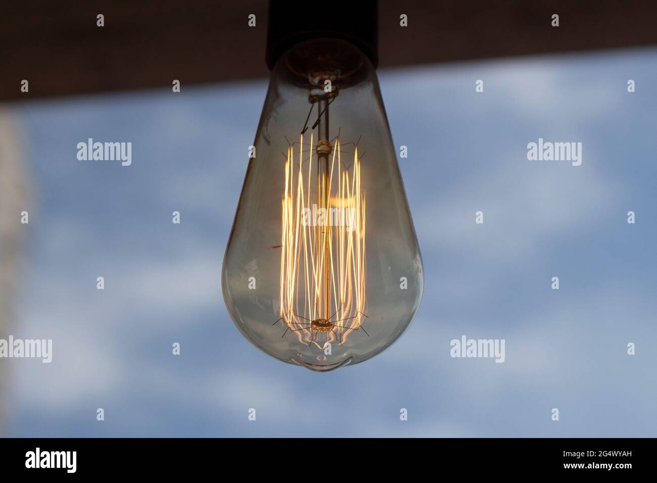 Glühlampe gegen den Himmel. Dekorative Lampe im Innenbereich. Ein altes Beleuchtungsgerät. Stockfoto