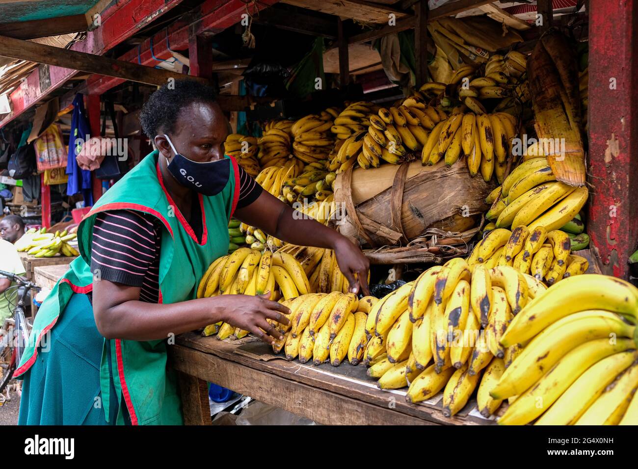 Kampala, Uganda. Juni 2021. Ein Verkäufer mit Gesichtsmaske arrangiert am 23. Juni 2021 auf einem Markt in Kampala, Uganda, süße Bananen. Eine virulente zweite Welle von COVID-19 zerstört das Land mit einer positiven Rate von 17.1 Prozent weiter. Quelle: Hascharah Nalwadda/Xinhua/Alamy Live News Stockfoto