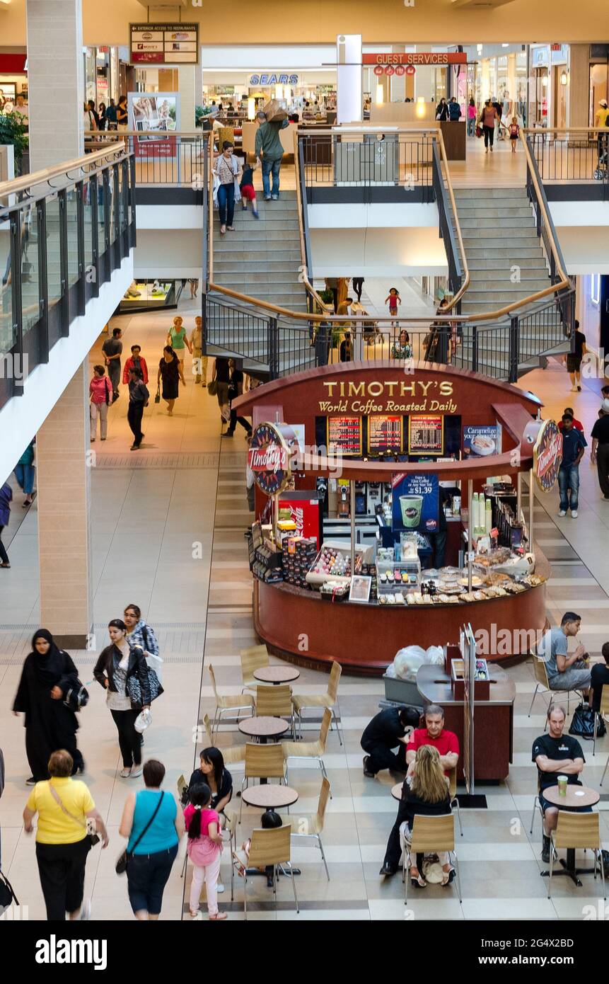 Menschen, die in der Halle eines großen Einkaufszentrums spazieren. Ein kleines Café Timothy's mit Besuchern. Stockfoto
