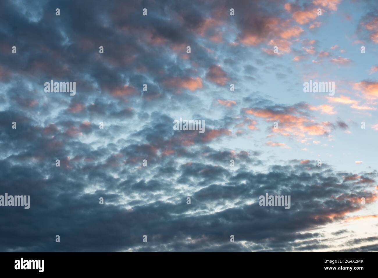 fotografie del cielo tormentoso y tranquilo con nubes cumulus estractus azules, blancas, naranjas y negra , con un molino de agua de fondo, horizontal Stockfoto