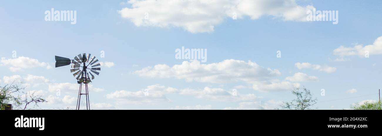 Fotografie del cielo tormentoso y tranquilo con nubes cumulus estractus azules, blancas, naranjas y negra , con un molino de agua de fondo, horizontal Stockfoto