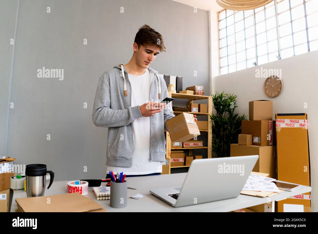 Der professionelle Mann scannt den Barcode auf der Verpackung vor dem Laptop am Schreibtisch Stockfoto