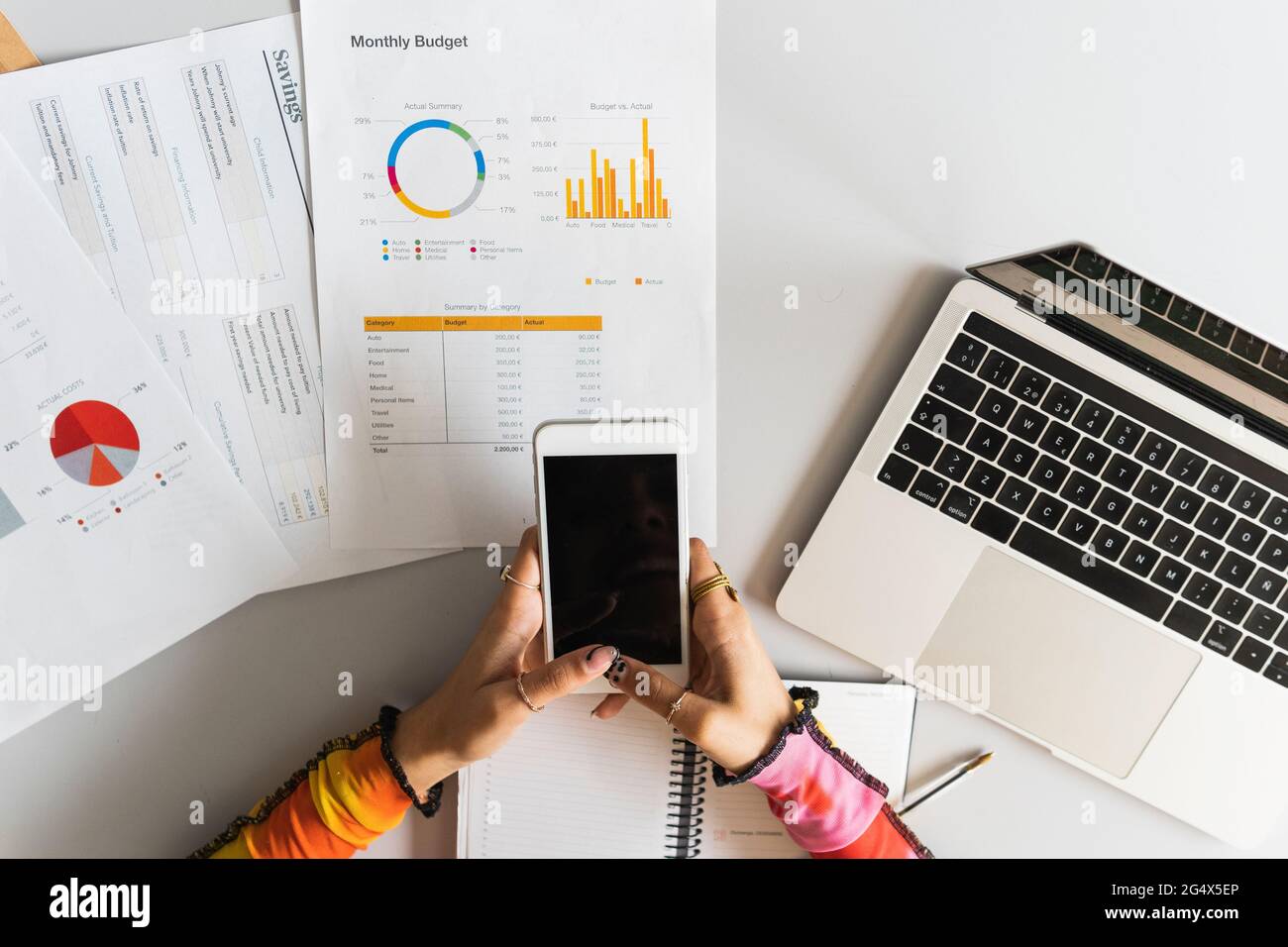 Frau, die per Finanzkarte auf dem Schreibtisch ein Mobiltelefon benutzt Stockfoto