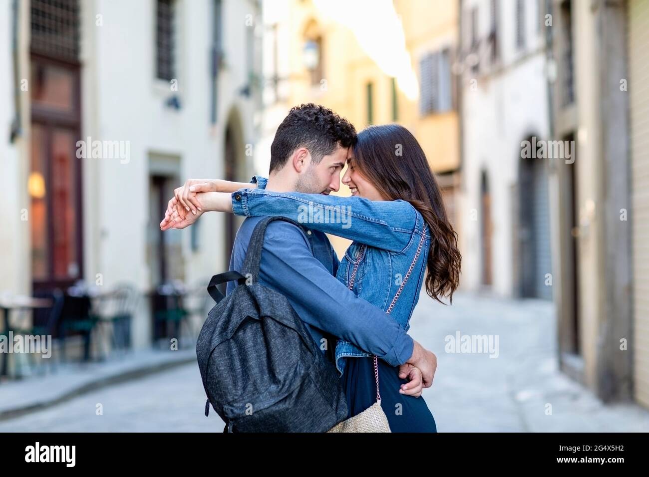 Lächelndes Paar, das auf der Straße der Stadt mit einem Gesicht und einem Arm um sich herum steht Stockfoto