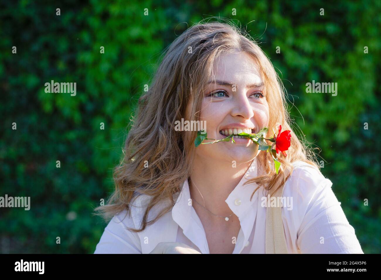 Junge Frau mit Freesia Blume im Mund wegschauen Stockfoto