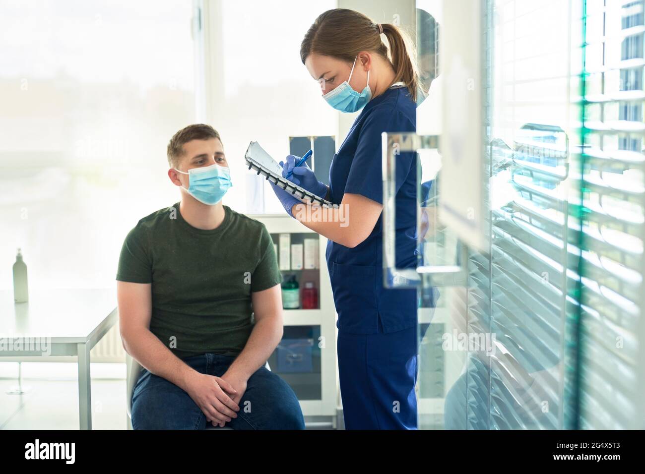 Arzt, der das Patienteninterview vor der Verabreichung des COVID-19-Impfstoffs in der Impfstelle abnimmt Stockfoto