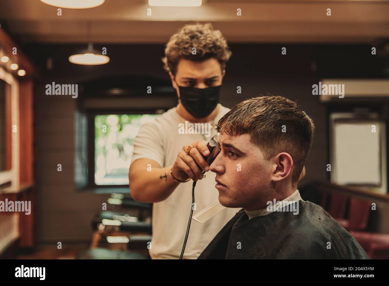 Junger Mann, der während des COVID-19-Ausbruchs vom männlichen Friseur im Salon einen Haarschnitt erhalten hat Stockfoto