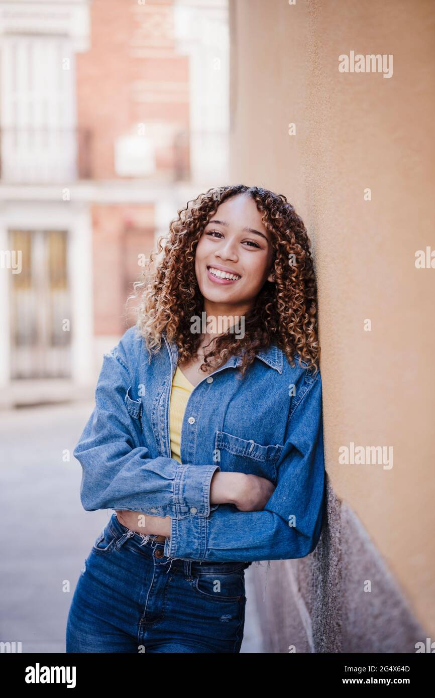 Lächelnde Frau mit gekreuzten Armen, die an der Wand gelehnt sind Stockfoto