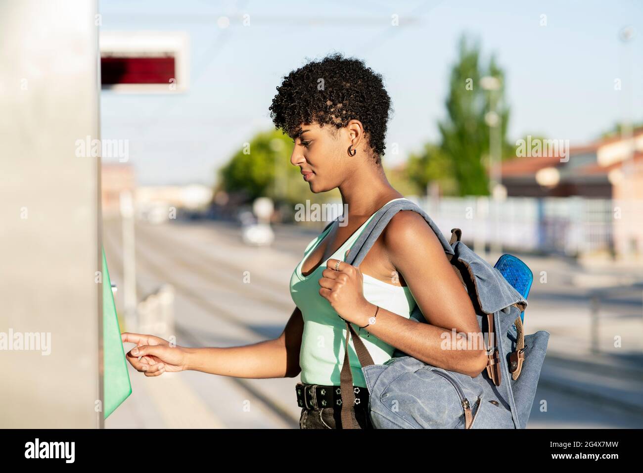 Junge Frau trägt Rucksack, während sie den Ticketautomaten benutzt Stockfoto