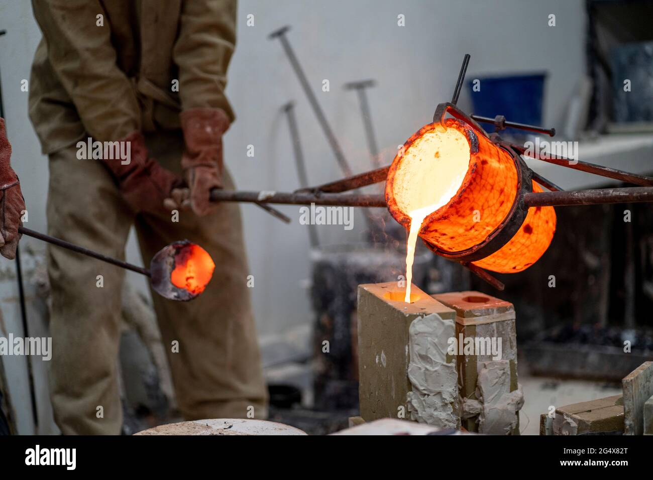 Manuelle Arbeiter gießen geschmolzene Bronze in Behälter in der Gießerei Stockfoto