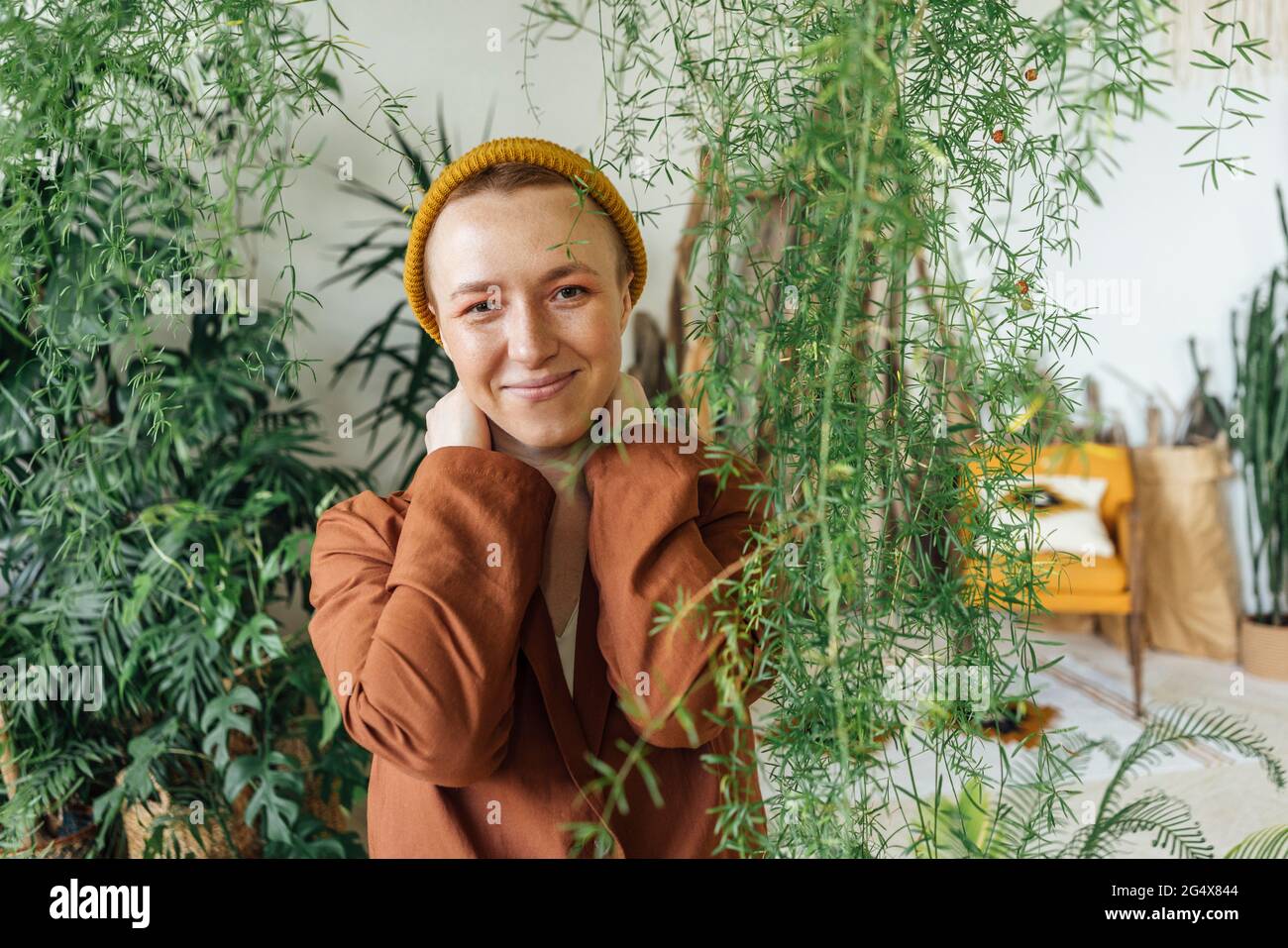 Lächelnde Geschäftsfrau trägt Strickmütze von Pflanzen im grünen Büro Stockfoto