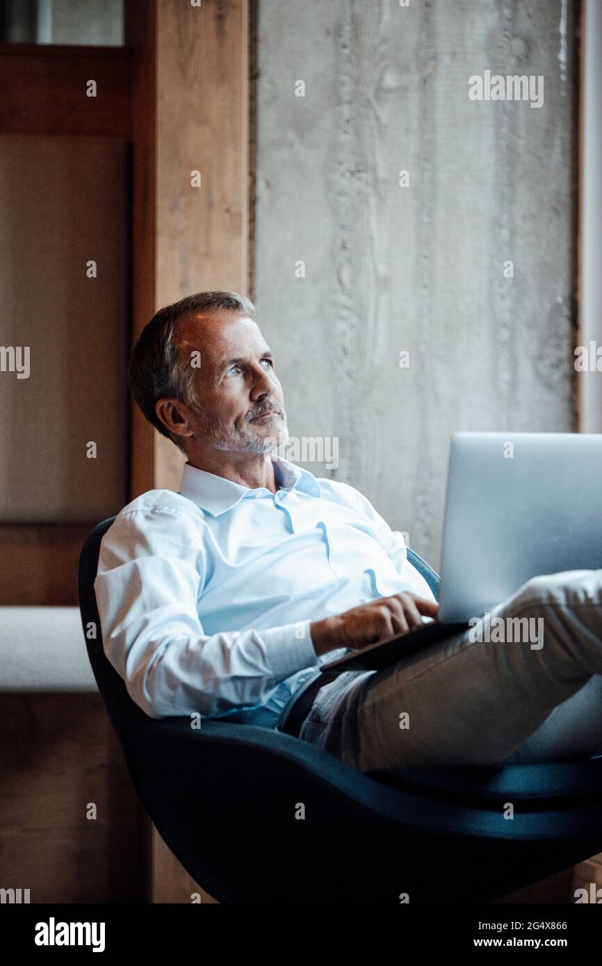 Leitender männlicher Unternehmer mit einem Laptop, der während der Betrachtung im Büro wegschaut Stockfoto