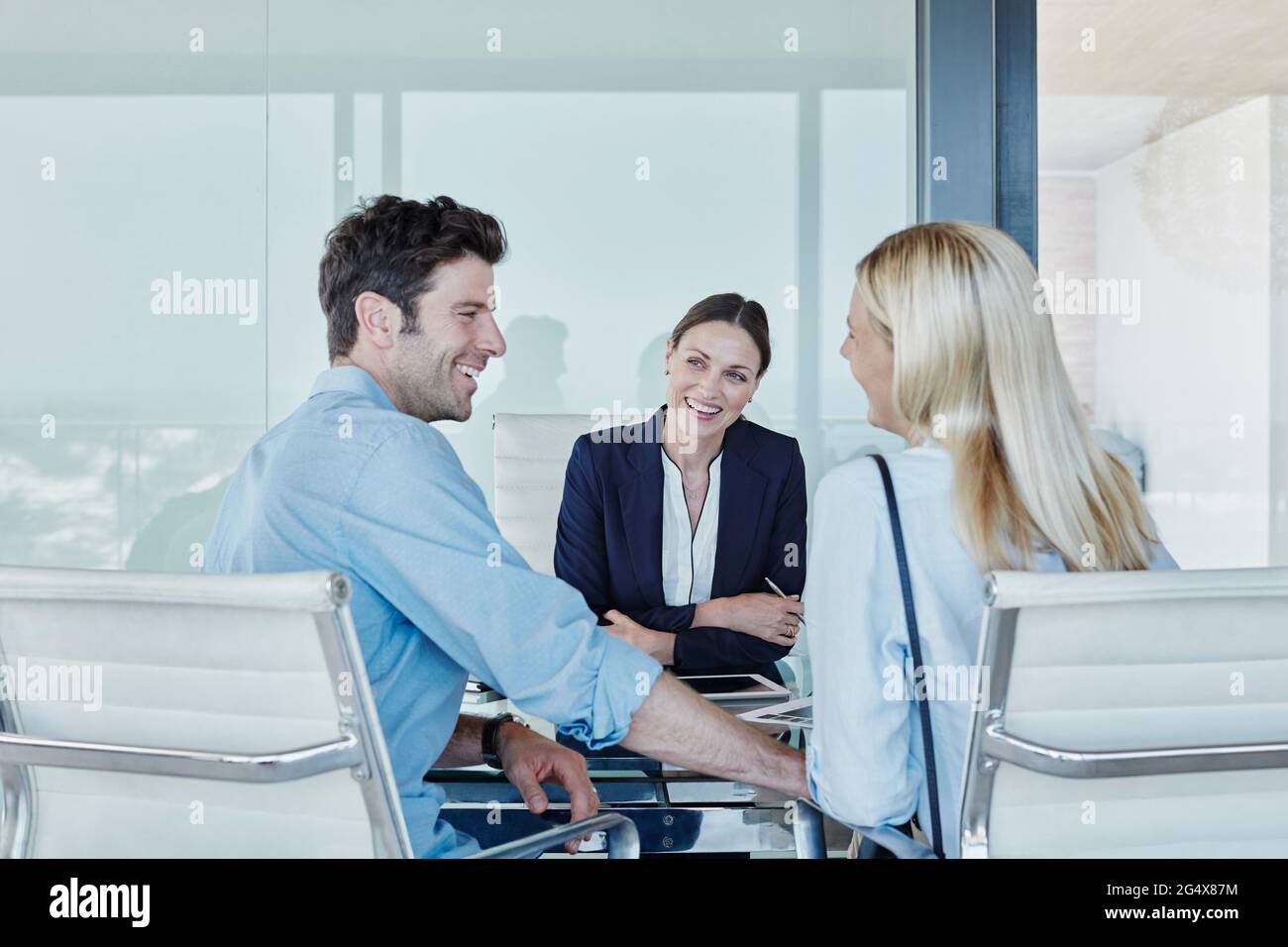 Lächelnde weibliche Immobilienmaklerin, die ein fröhliches Paar am Tisch sieht Stockfoto